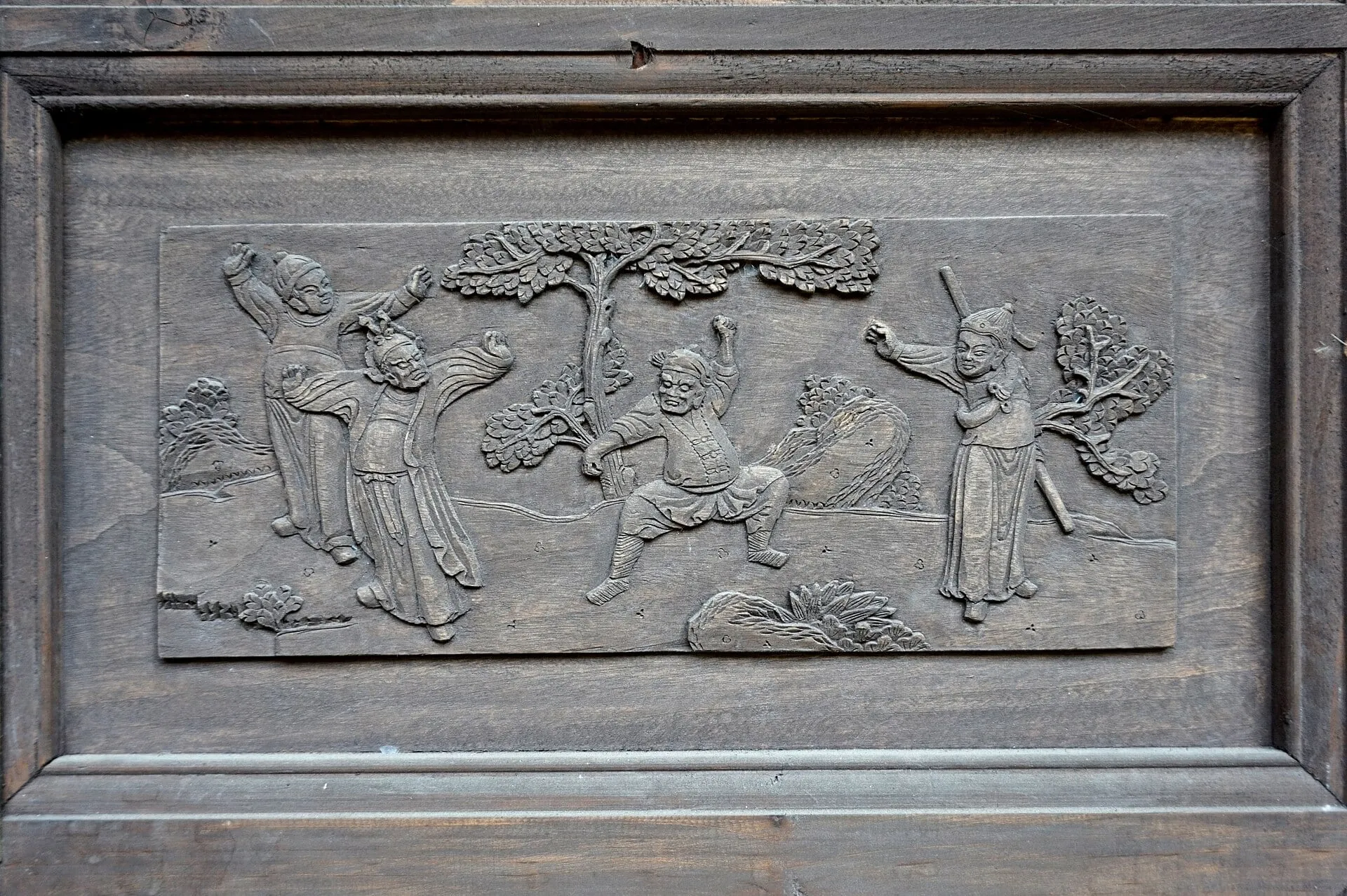 A carved wooden panel in the Wenyuan courtyard house, with figures beneath trees.
